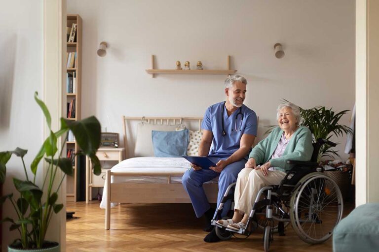 An older adult sitting with a caregiver, reviewing medication and health records at a dining table.